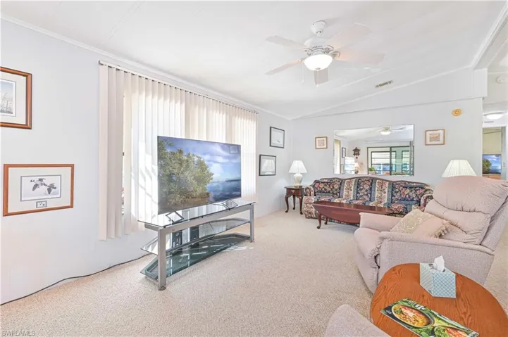 Carpeted living area featuring ceiling fan, vaulted ceiling, and crown molding