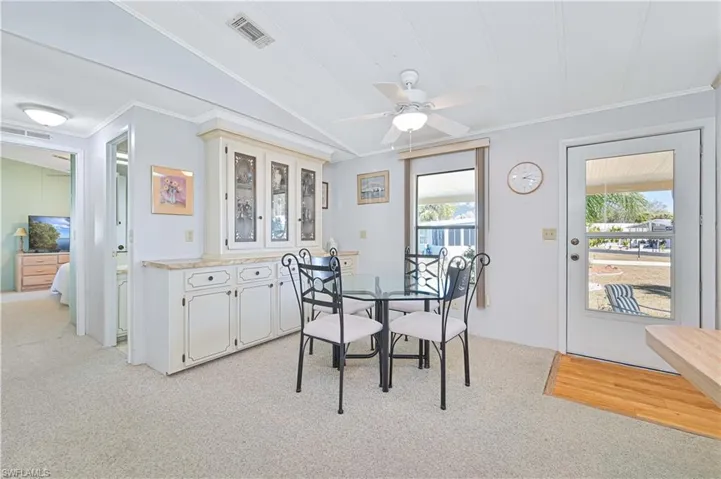 Dining space with a ceiling fan, lofted ceiling, light carpet, and crown molding