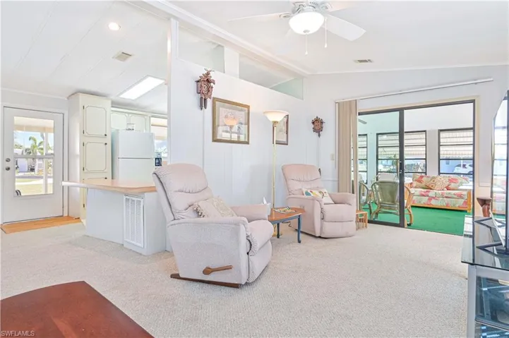 Living area featuring light colored carpet, vaulted ceiling, and a ceiling fan