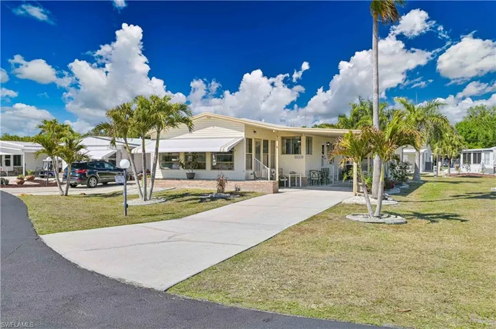 Manufactured / mobile home featuring driveway, an attached carport, a front yard, and covered porch