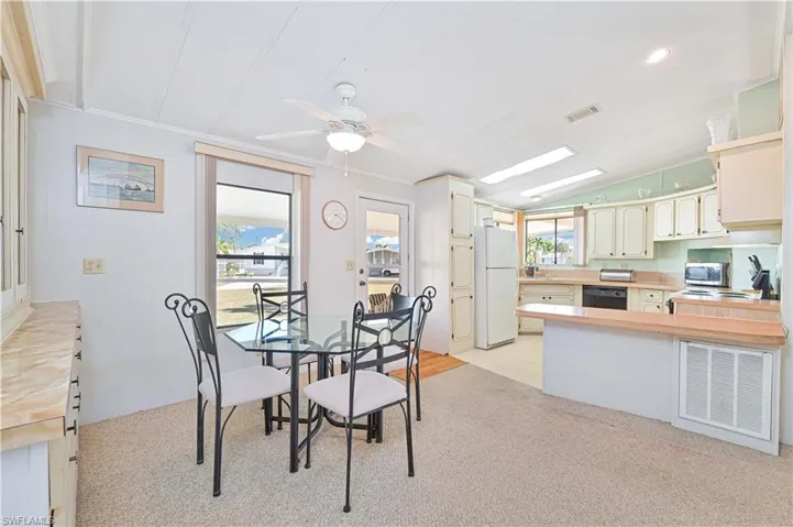 Dining space with ceiling fan, light colored carpet, and vaulted ceiling