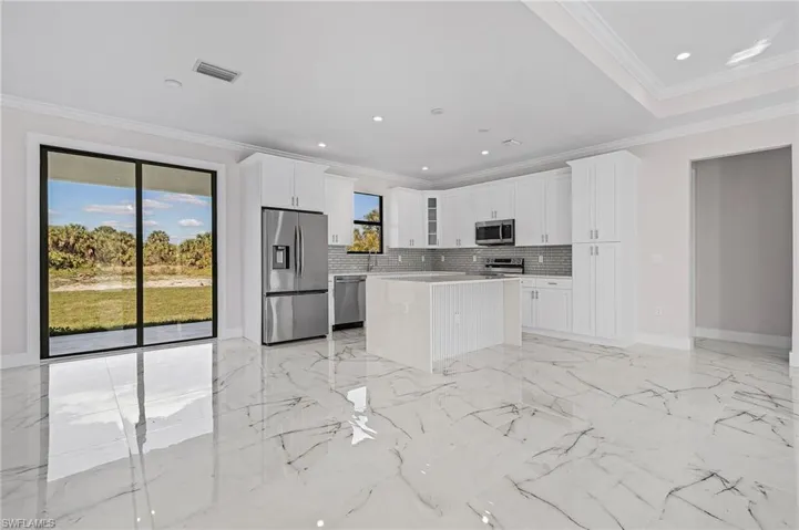 Kitchen with crown molding, tasteful backsplash, a kitchen island, stainless steel appliances, and white cabinets