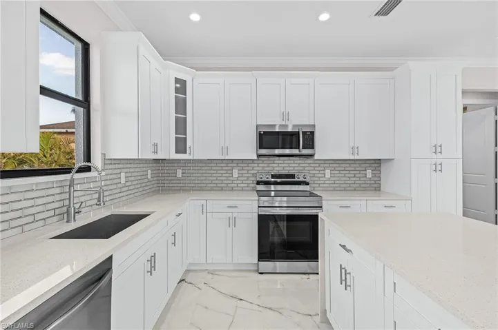 Kitchen with white cabinetry, sink, ornamental molding, light stone counters, and stainless steel appliances