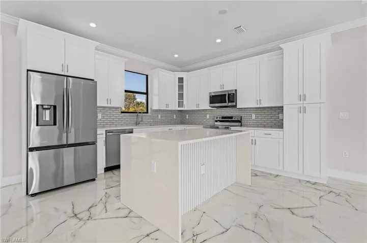Kitchen featuring crown molding, backsplash, stainless steel appliances, white cabinets, and a kitchen island