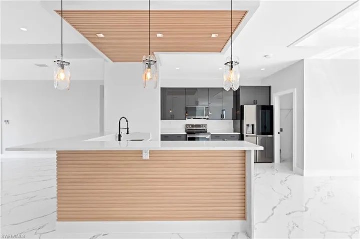 Kitchen featuring a kitchen breakfast bar, pendant lighting, stainless steel appliances, light stone counters, and a large island with sink