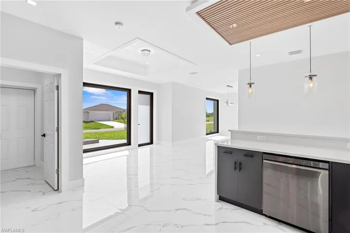 Kitchen featuring stainless steel dishwasher, healthy amount of natural light, decorative light fixtures, light stone counters, and a tray ceiling