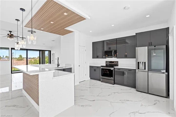 Kitchen with stainless steel appliances, a peninsula, hanging light fixtures, a ceiling fan, and light stone countertops