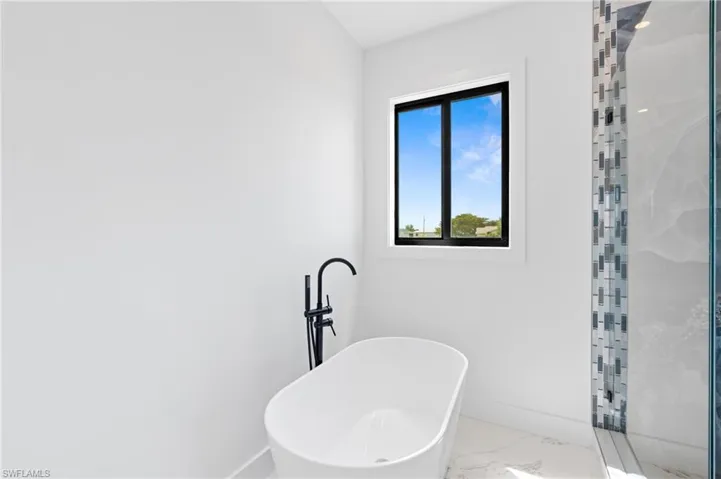 Bathroom featuring marble look tile flooring, a freestanding bath, and a shower stall