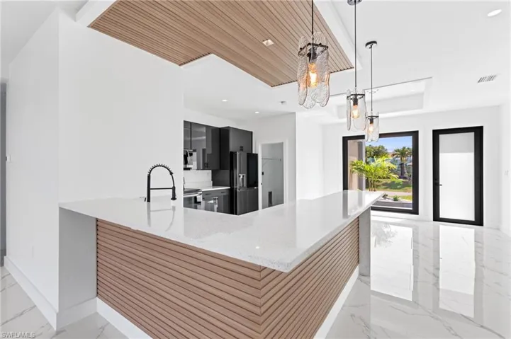 Kitchen with dark cabinets, a peninsula, light stone countertops, refrigerator with ice dispenser, and light marble finish floors