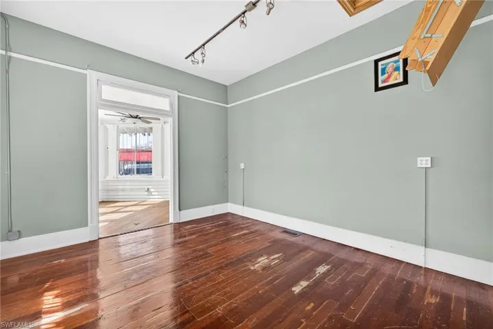 Empty room with dark wood finished floors, rail lighting, and a ceiling fan