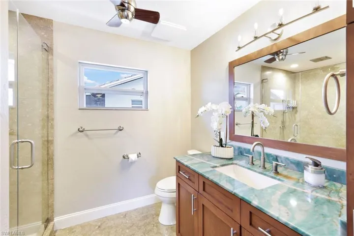 Bathroom featuring a shower with door, vanity, ceiling fan, and toilet