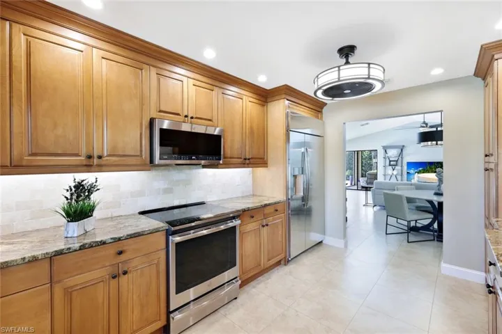 Kitchen featuring lofted ceiling, appliances with stainless steel finishes, light stone countertops, and decorative backsplash