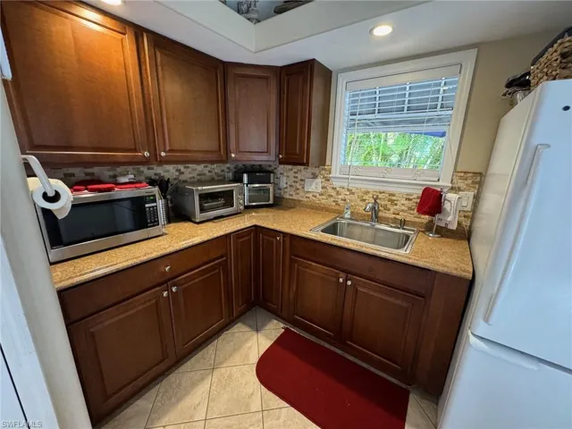 Kitchen with backsplash, sink, white fridge, and light tile patterned floors