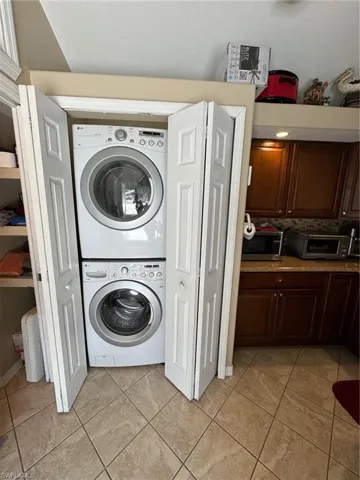 Washroom featuring stacked washer / drying machine and light tile patterned flooring