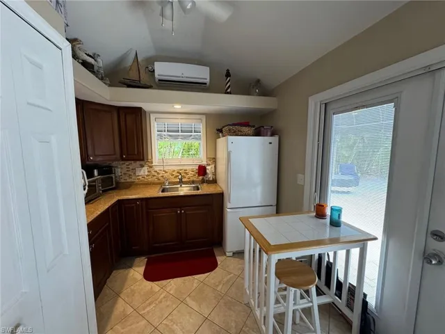 Kitchen with sink, tasteful backsplash, white refrigerator, an AC wall unit, and light tile patterned floors
