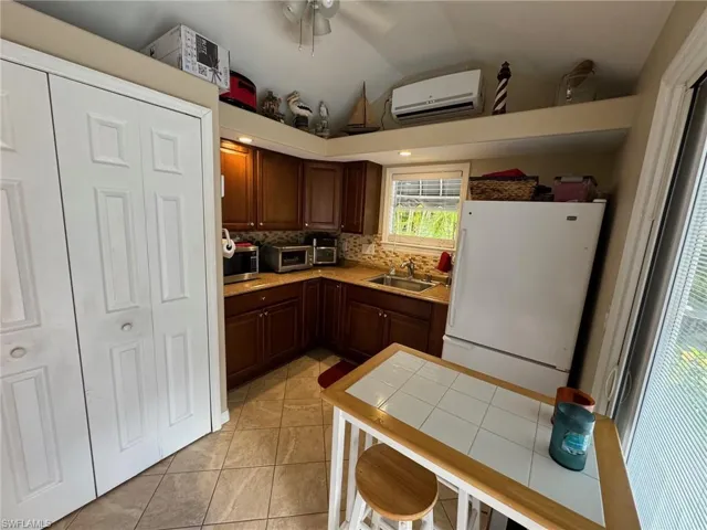 Kitchen with white refrigerator, sink, decorative backsplash, a wall mounted AC, and light tile patterned flooring