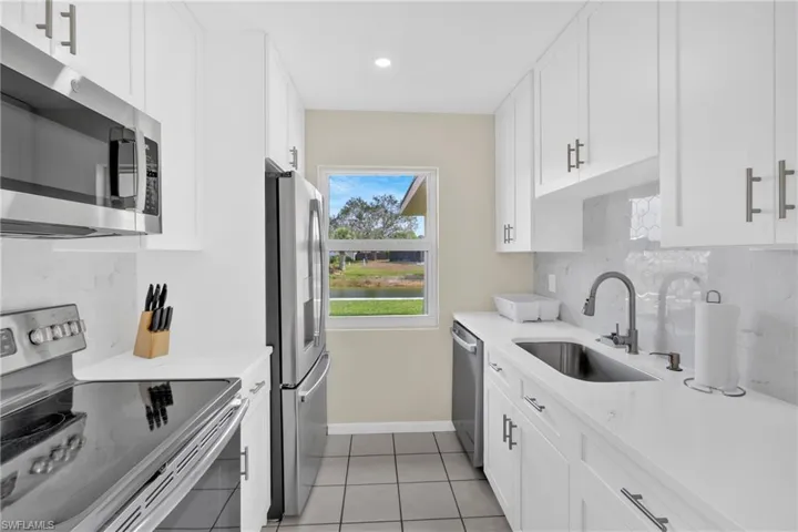 Kitchen with stainless steel appliances, white cabinets, decorative backsplash, light stone counters, and recessed lighting