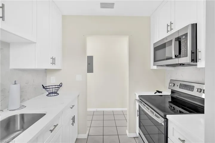 Kitchen with tasteful backsplash, appliances with stainless steel finishes, white cabinets, light stone countertops, and electric panel