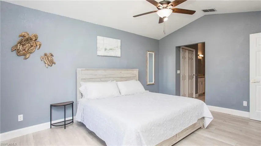 Bedroom with light wood-type flooring, ensuite bathroom, vaulted ceiling, and ceiling fan