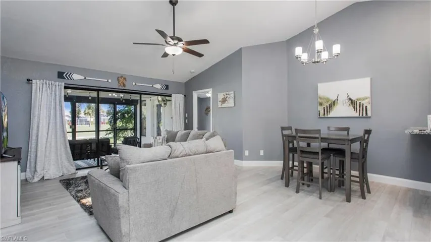 Living room featuring ceiling fan with notable chandelier, lofted ceiling, and light hardwood / wood-style flooring