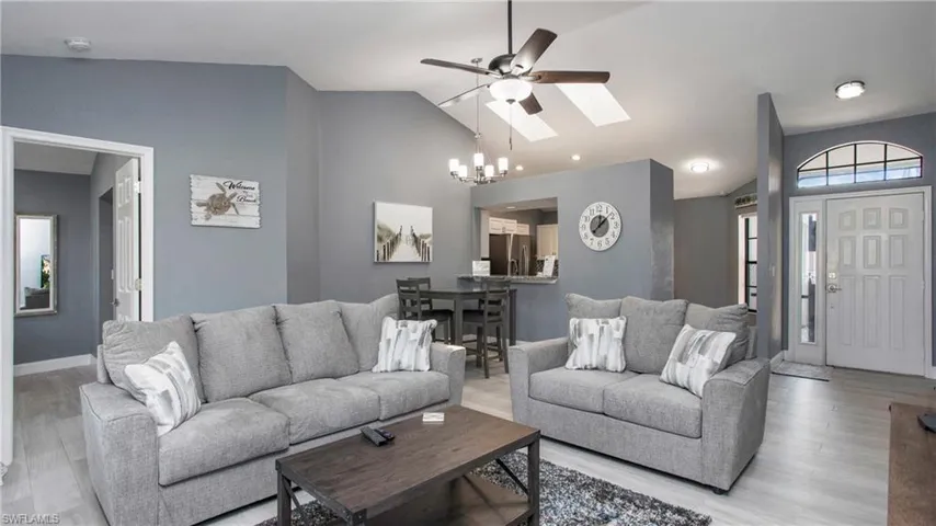Living room featuring lofted ceiling with skylight, light hardwood / wood-style floors, and ceiling fan with notable chandelier