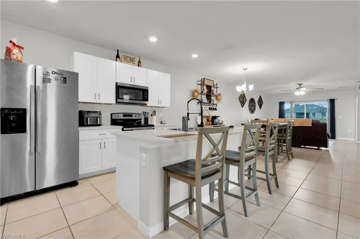 Kitchen with stainless steel appliances, a kitchen breakfast bar, light tile patterned flooring, a center island with sink, and white cabinets