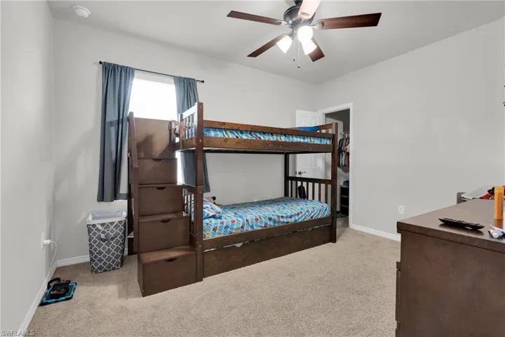 Bedroom featuring light carpet, a spacious closet, and a ceiling fan
