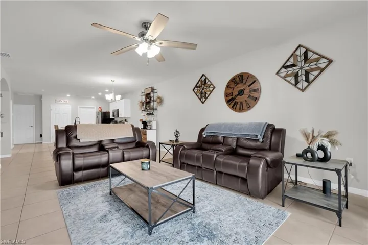 Living area with light tile patterned flooring, a ceiling fan, hanging lights, and arched walkways