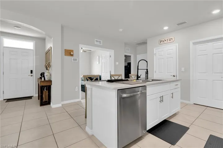 Kitchen featuring dishwasher, light tile patterned flooring, white cabinets, a kitchen island with sink, and arched walkways