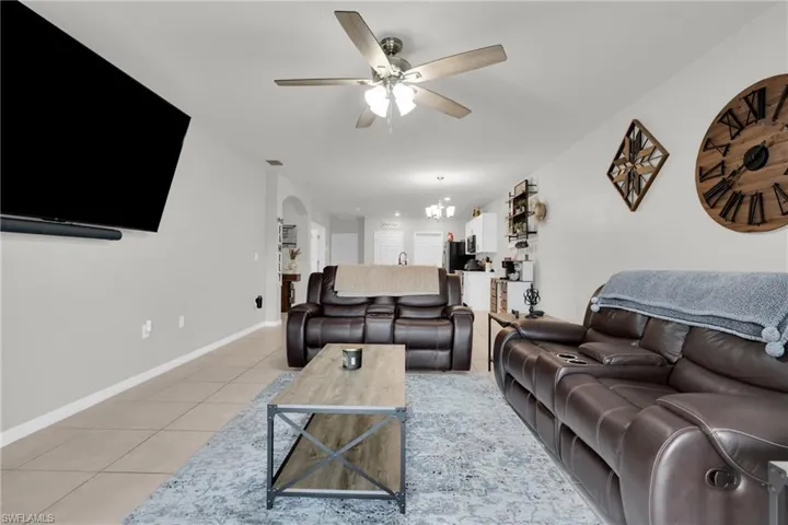 Living room featuring light tile patterned floors, a ceiling fan, arched walkways, and hanging lights