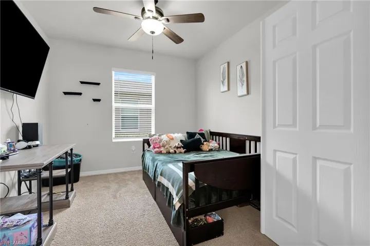 Bedroom featuring light carpet, a ceiling fan, and a desk