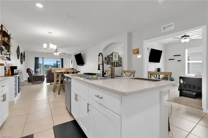Kitchen with a ceiling fan, a breakfast bar area, an island with sink, open floor plan, and white cabinetry