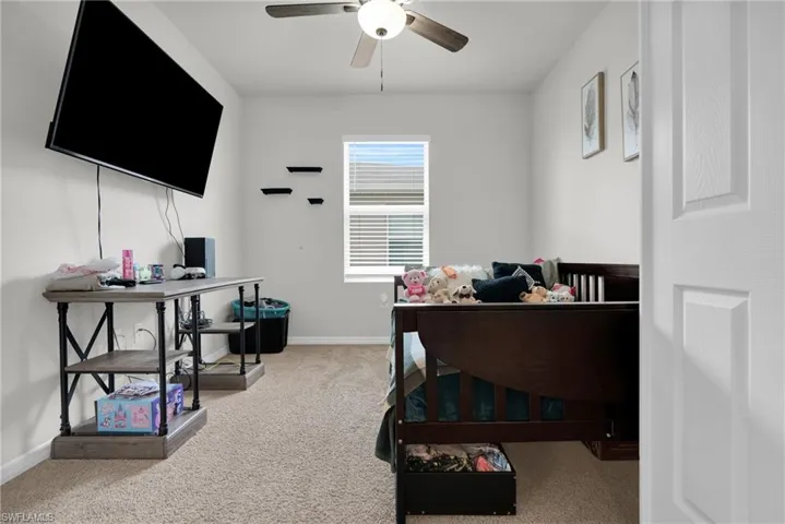 Bedroom with an office area, light colored carpet, and a ceiling fan
