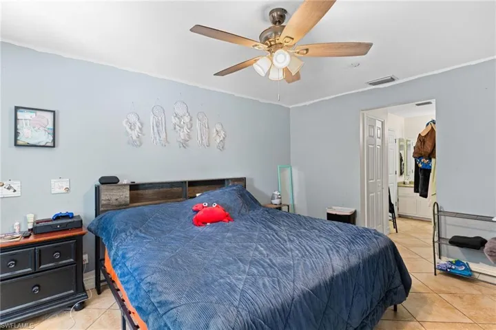 Bedroom with ornamental molding, light tile patterned floors, and a ceiling fan