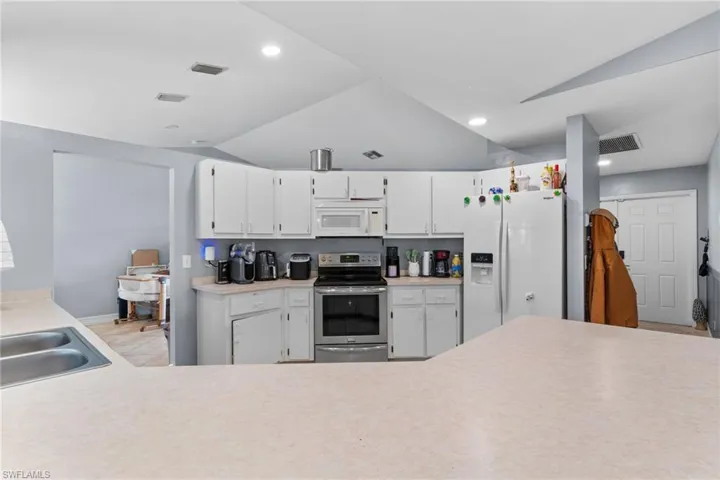 Kitchen featuring lofted ceiling, white cabinetry, light countertops, and white appliances