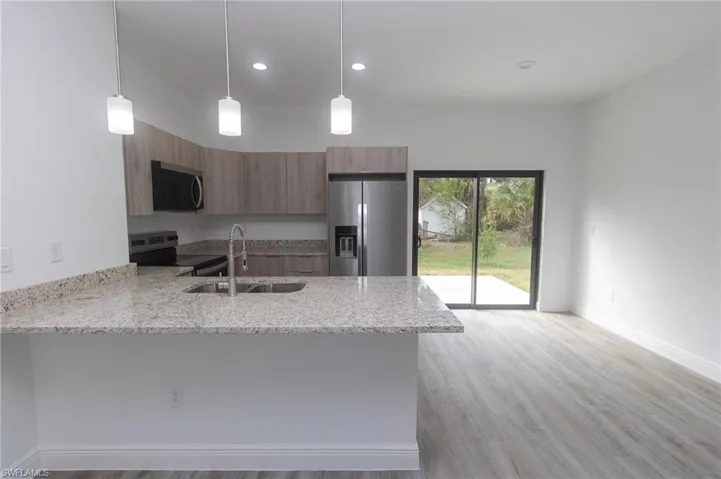 Kitchen with brown cabinetry, modern cabinets, appliances with stainless steel finishes, a peninsula, and a sink