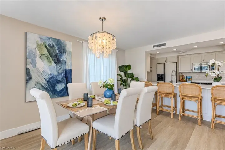 Kitchen featuring white cabinetry, stone-finish countertops, stainless steel appliances, and a breakfast bar with wood-finish flooring and a decorative multi-tiered pendant light