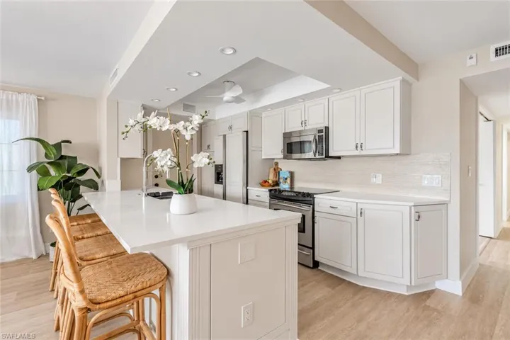 Kitchen featuring a central island with a solid surface countertop, white shaker-style cabinetry, stainless steel appliances, recessed ceiling lighting, and wood-finish flooring