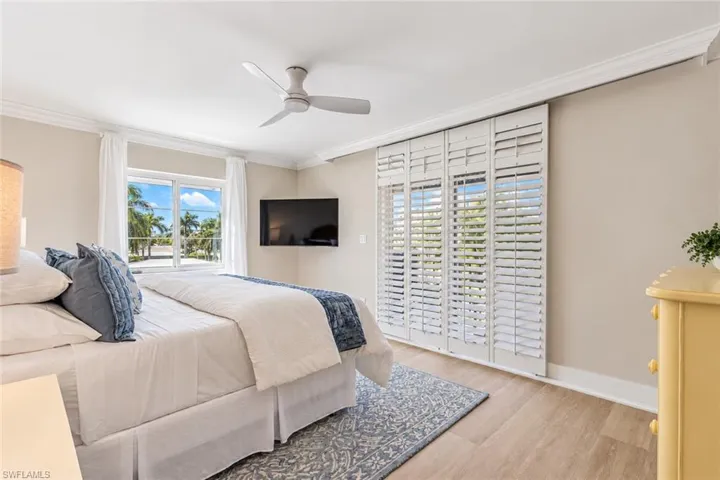 Neutral interior featuring wood-finish flooring, crown molding, a ceiling fan, and white plantation shutters