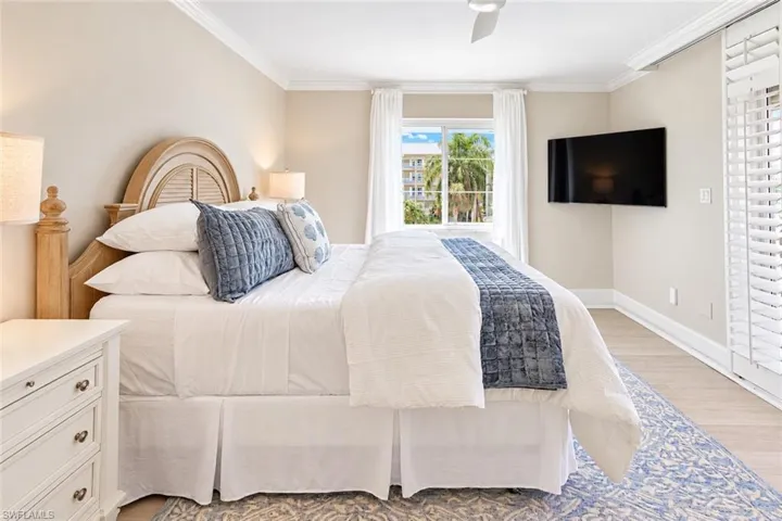 Neutral-toned bedroom featuring wood-finish flooring, crown molding, white plantation shutters, and a ceiling fan