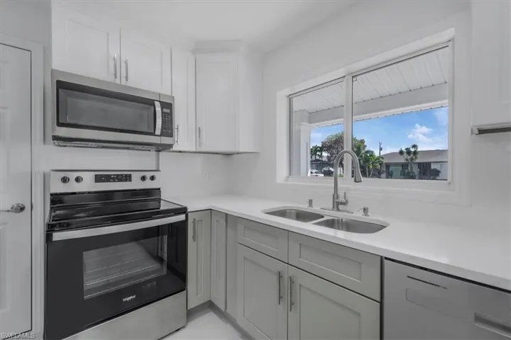 Kitchen featuring stainless steel appliances, white cabinets, gray cabinetry, and light stone counters