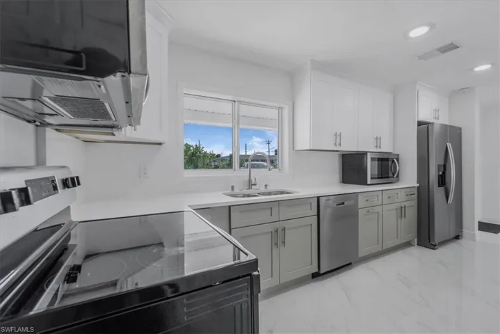 Dual tone kitchen with stainless steel appliances, extractor fan, dual tone cabinets, light marble finish flooring, and recessed lighting