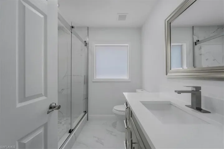 Bathroom with vanity, a marble finish shower, and light marble finish floors