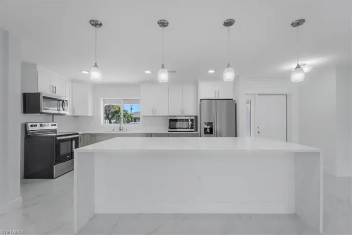 Kitchen featuring stainless steel appliances, white cabinetry, a large island, and light stone countertops
