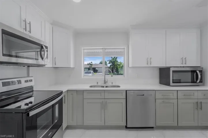 Kitchen featuring stainless steel appliances, dual tone cabinetry, and light stone counters