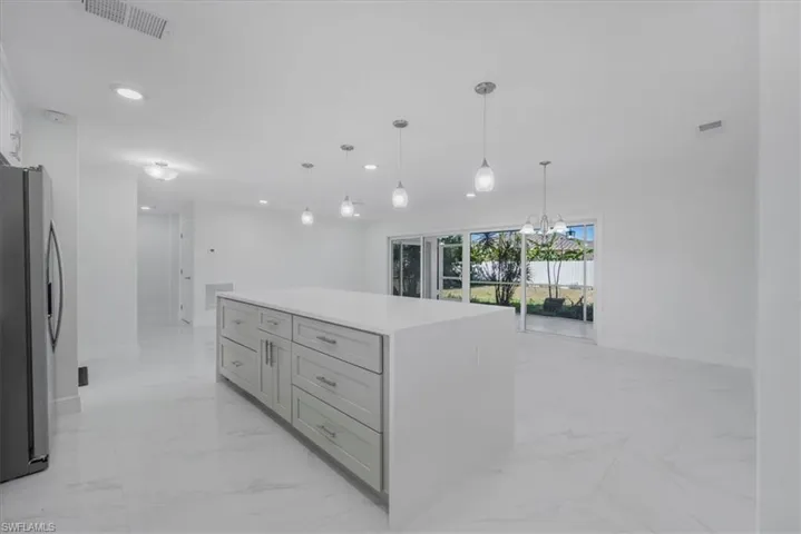 Kitchen with a center island, freestanding refrigerator, light stone counters, suspended lighting, and gray cabinets
