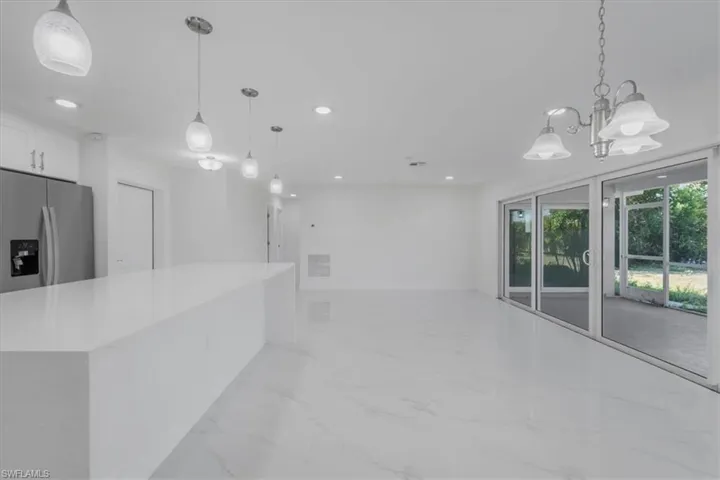 Kitchen with stainless steel refrigerator with ice dispenser, white cabinets, light stone countertops, open floor plan, and light marble finish floors