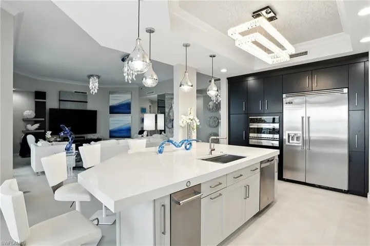 Kitchen featuring ornamental molding, a raised ceiling, a breakfast bar, stainless steel appliances, and decorative light fixtures - Virtually Edited Image