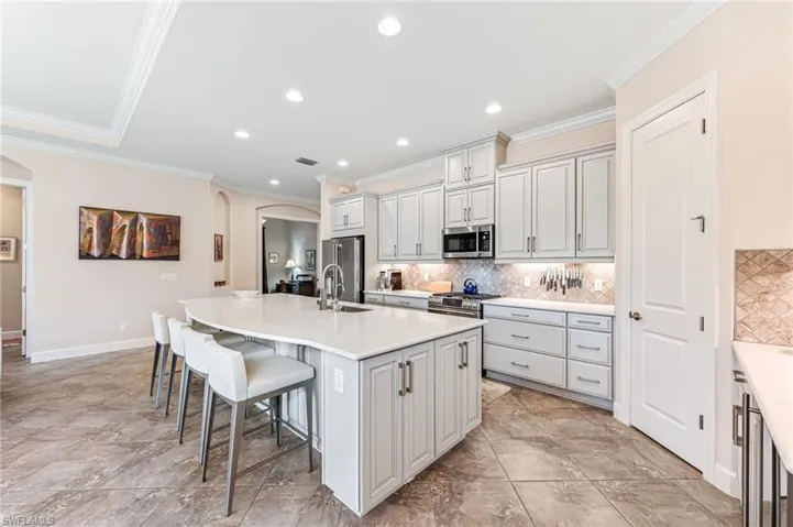 Kitchen featuring decorative backsplash, an island with sink, a breakfast bar area, arched walkways, and stainless steel appliances