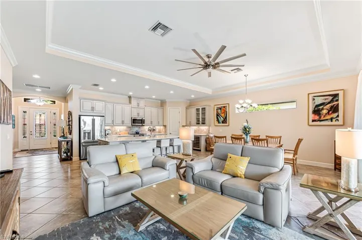 Living area featuring ornamental molding, ceiling fan with notable chandelier, visible vents, and a raised ceiling